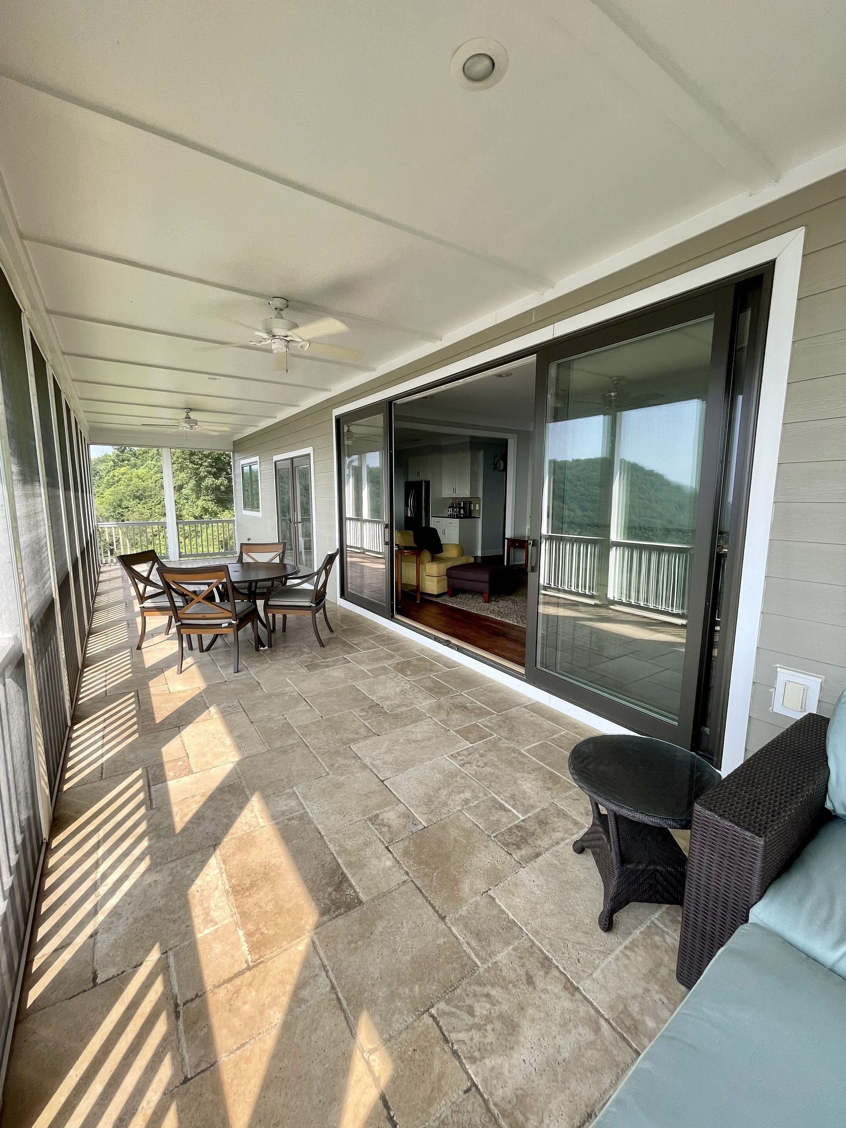 A covered patio with a dining area, a sofa, and a sliding glass door leading to a living room.