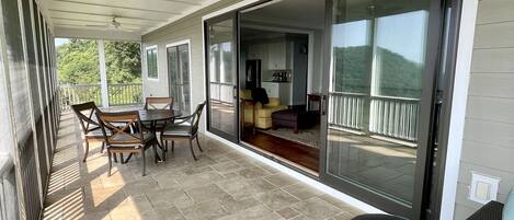 A covered patio with a dining area, a sofa, and a sliding glass door leading to a living room.