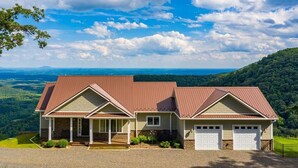 A two-story house with a brown roof and beige siding, located on a hill with a view of a valley and mountains. - Mountain House located on Blue Ridge Parkway  (Galax)