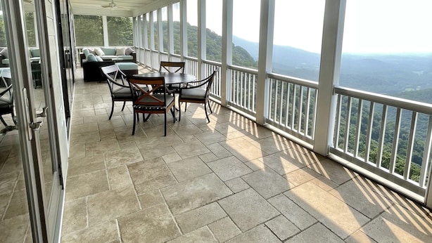A covered balcony with a table and chairs, large windows offering a view of the landscape, and a ceiling fan. - Mountain House located on Blue Ridge Parkway  (Galax)