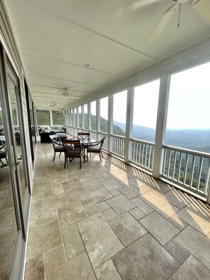 A covered balcony with a table and chairs, large windows offering a view of the landscape, and a ceiling fan. - Mountain House located on Blue Ridge Parkway  (Galax)