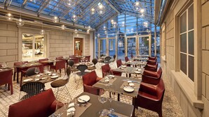 A spacious restaurant with a glass ceiling, multiple dining tables, and red chairs.
