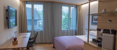A modern hotel room with a bed, a desk, a chair, and a large window with curtains.
