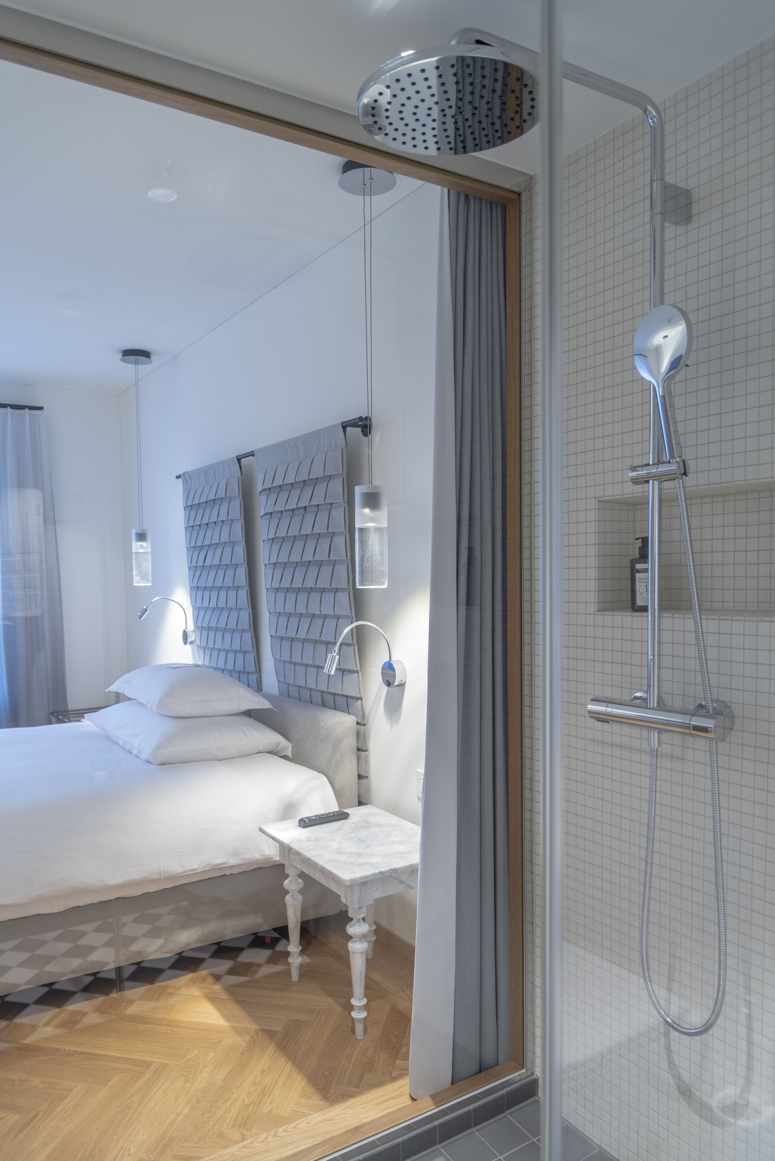 A modern hotel room with a large bed, a bedside table, a shower area, and a view of the city through the window.