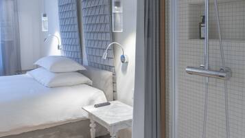 A modern hotel room with a large bed, a bedside table, a shower area, and a view of the city through the window.