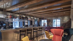 A bar area with wooden beams, bar stools, and a variety of bottles and glasses on shelves.