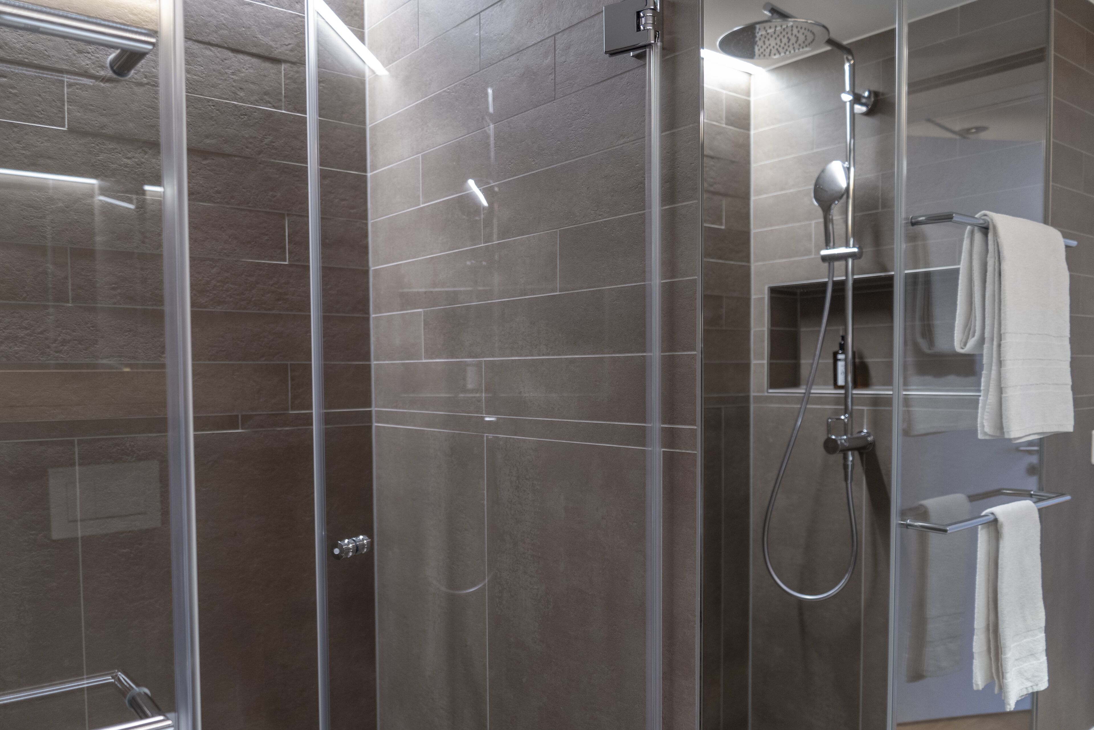 A modern shower area with a glass door, a handheld showerhead, and a towel rack with a white towel.