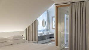A modern bedroom with a large bed, a bathroom with a vanity and mirrors, and a glass shower area.