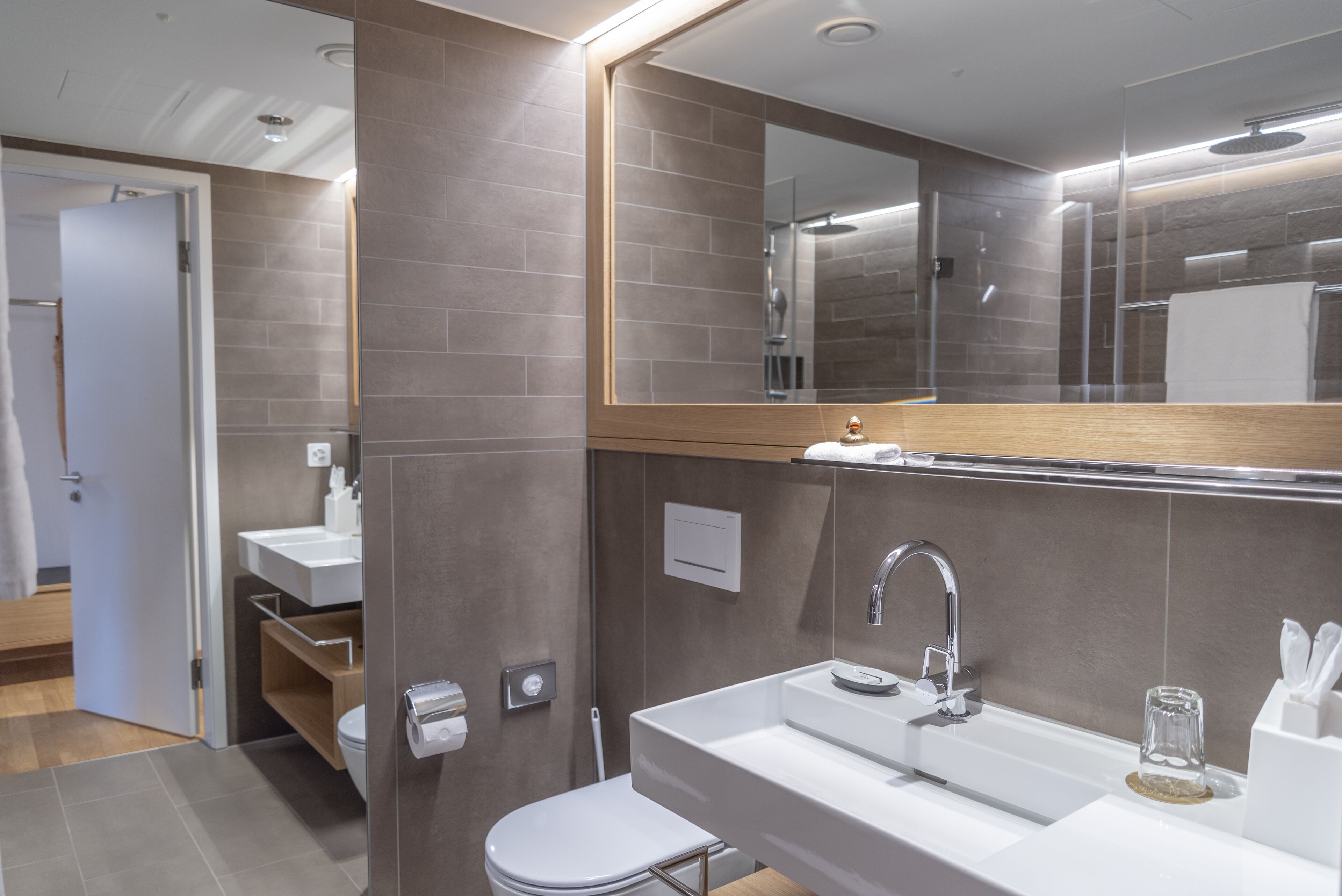 Un baño moderno con un espejo grande, un lavabo blanco y un inodoro.