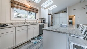 A modern kitchen with white cabinets, a granite countertop, a built-in dishwasher, and a large island with bar stools. - Fripp Island/Multi Family Friendly/ Dog Friendly/Spacious 3rd Row home/6 Seater Golf cart incl/-703 Amberjack (Fripp Island)