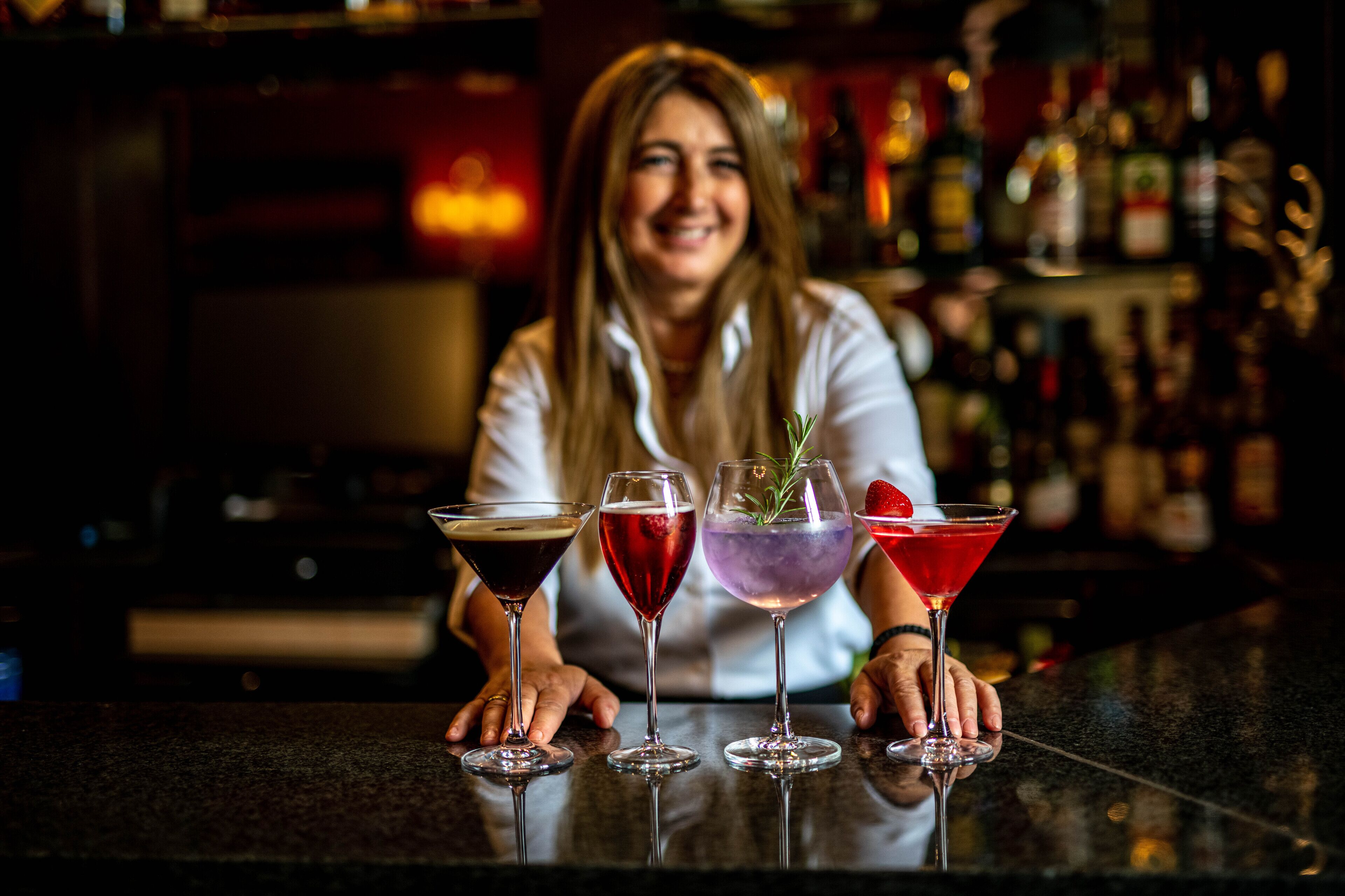 A bar with three cocktails and a bartender.