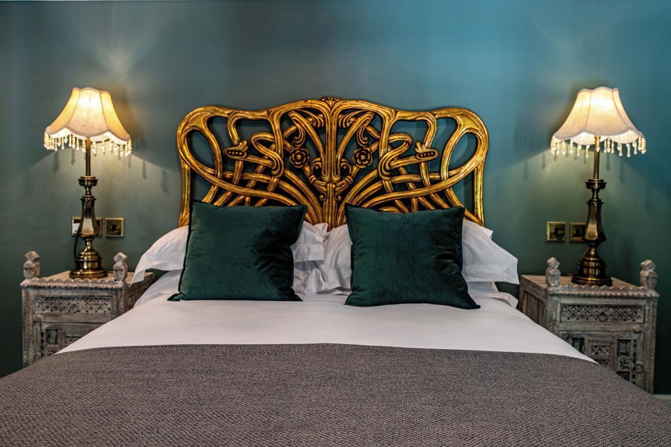 A bed with a decorative headboard, two bedside lamps, and two green pillows.