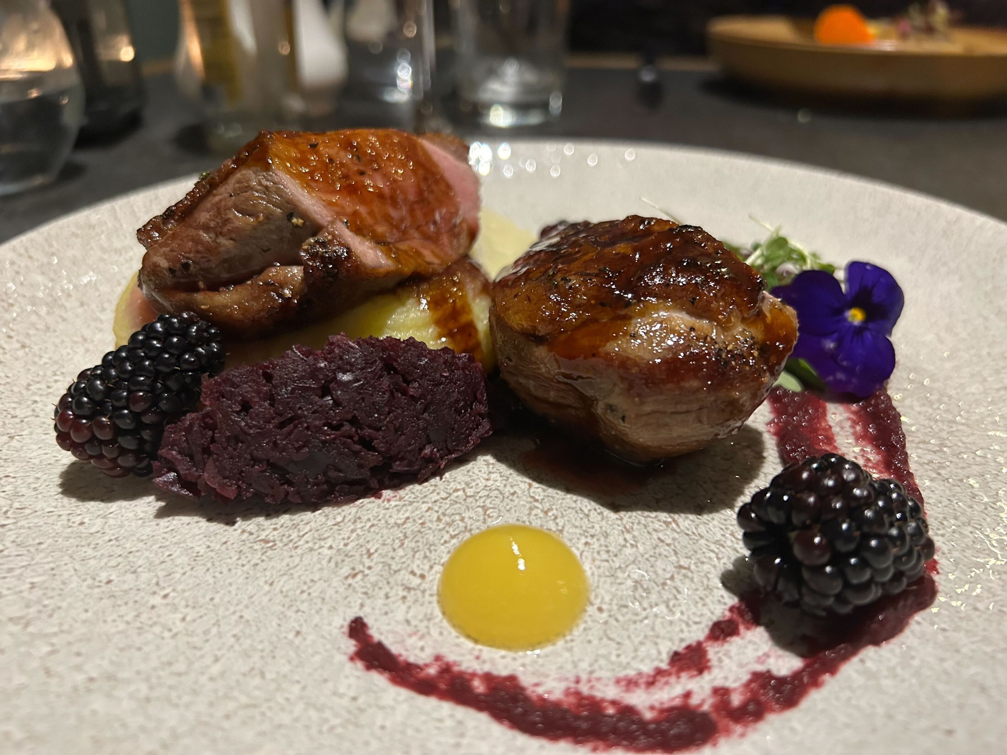 A plate of food with a piece of meat, a slice of cake, and a berry.