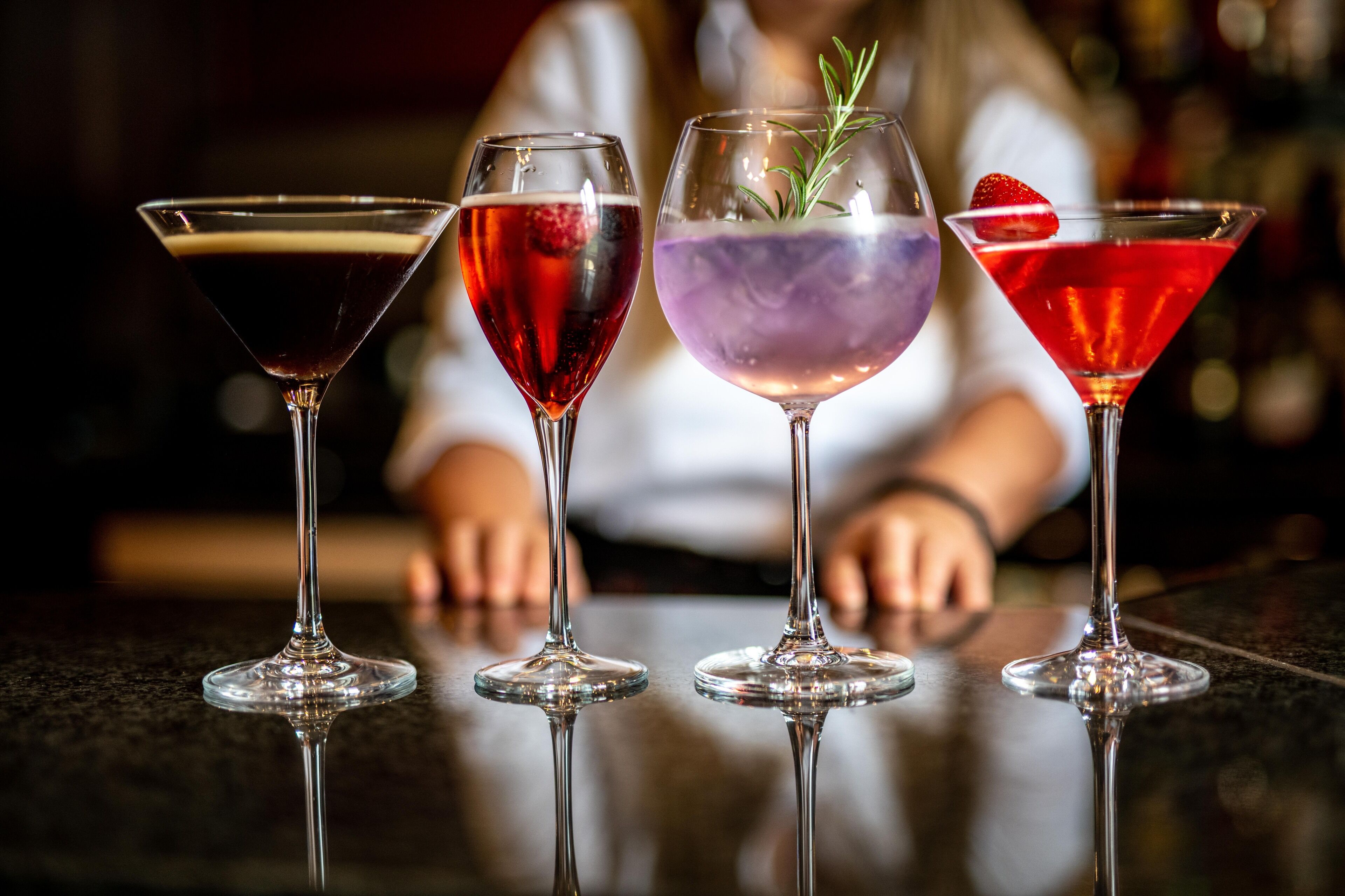 Four martini glasses with different colored drinks on a reflective surface.