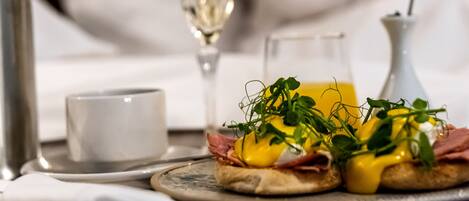 A breakfast tray with eggs benedict, a glass of champagne, and a small vase with a blue flower.