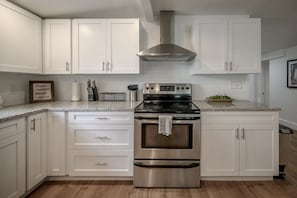 Una cocina con gabinetes blancos, estufa de acero inoxidable y campana extractora.