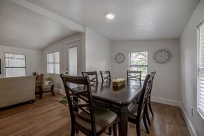 Un área de comedor con una mesa y sillas de madera, un sofá y dos obras de arte decorativas en las paredes.