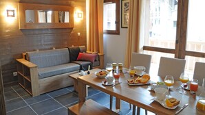 Una habitación acogedora con un sofá de madera, una mesa de comedor con desayuno servido y ventanas grandes con cortinas.