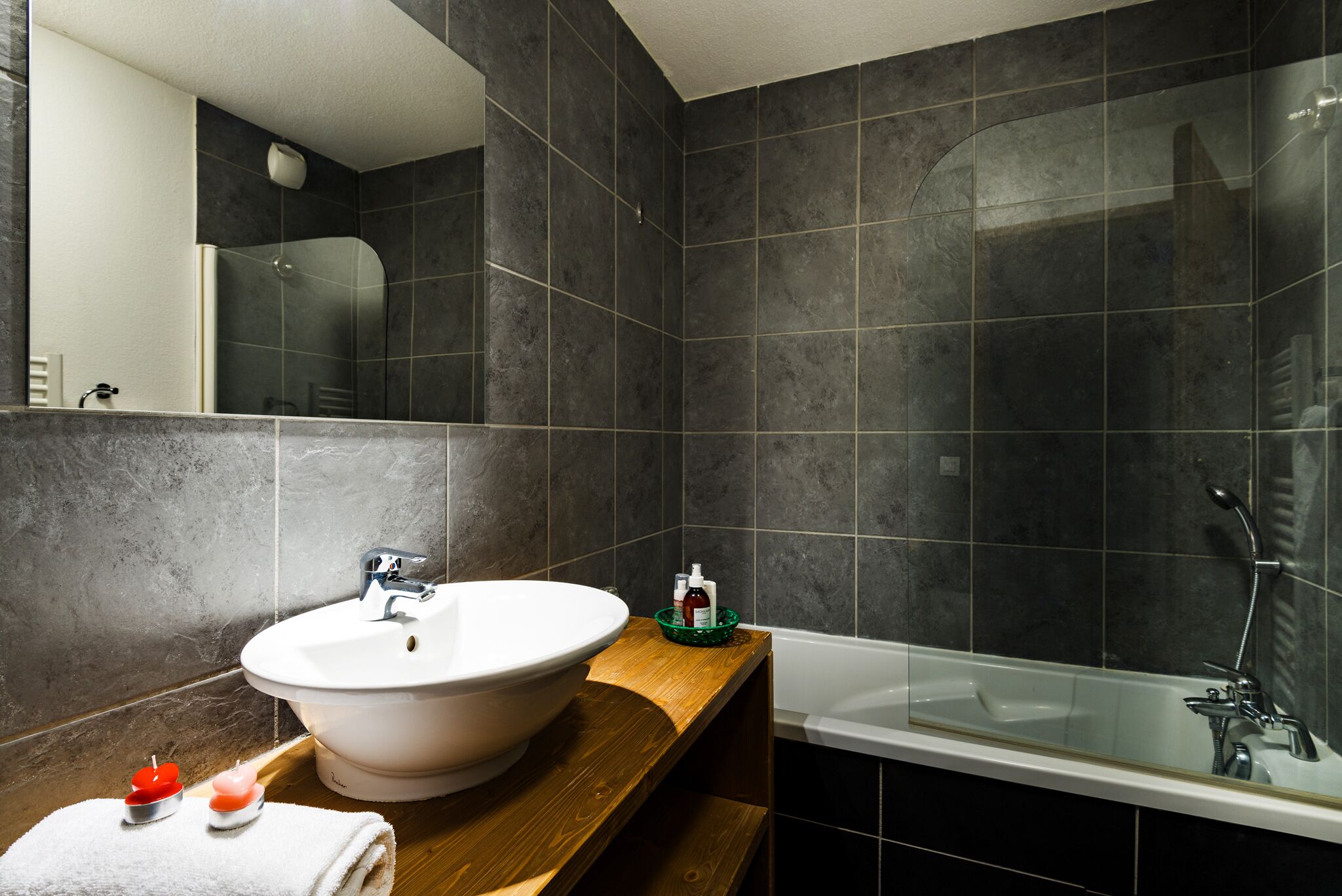 Ein modernes Badezimmer mit einem großen weißen Waschbecken, einer gläsernen Duschkabine und dunkel gefliesten Wänden.