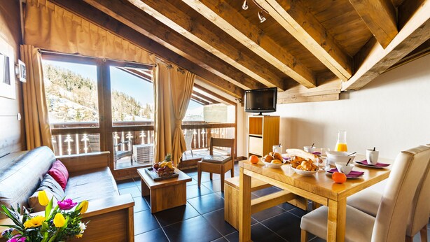 Una habitación acogedora con techo de madera, un sofá, una mesa de comedor con provisiones para el desayuno y un televisor.