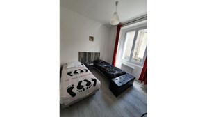 A bedroom with a bed, a bench, a window, and a wall-mounted light fixture. - La Belle Auvergne 2 / Ground floor F3 - 5 people (Condat)