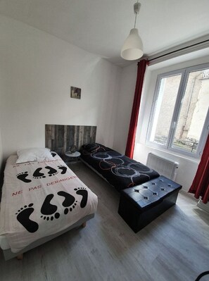 Een slaapkamer met een bed, een bankje, een raam en een wandlamp.
