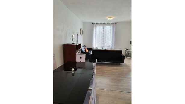 Ein modernes Wohnzimmer mit Holzboden, einer schwarzen Couch, einem Holzschrank und einem kleinen Tisch mit Lampe.