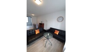 Ein modernes Wohnzimmer mit einer schwarzen Ledersofa, einem Glastisch und einer Wanduhr.