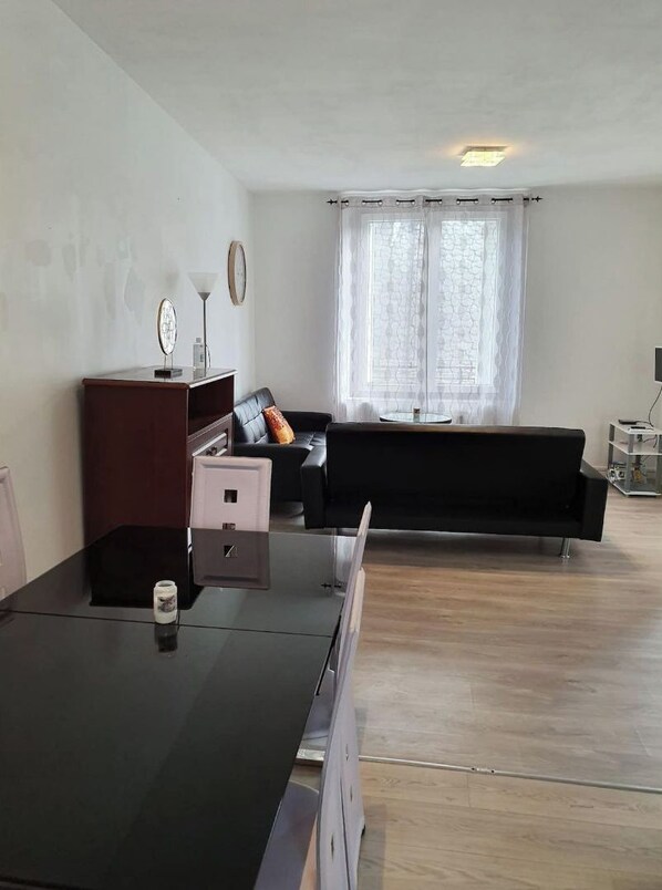 Un salon moderne avec un plancher en bois, un canapé noir, un meuble en bois et une petite table avec une lampe.