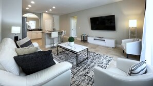 Ein modernes Wohnzimmer mit Sofa, Sesseln, Couchtisch und einem an der Wand montierten Fernseher.