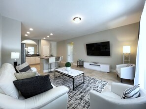 A modern living room with a sofa, armchair, coffee table, and a TV mounted on the wall.