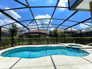 A swimming pool with a clear blue water, surrounded by a covered area with a metal frame and a tiled floor.