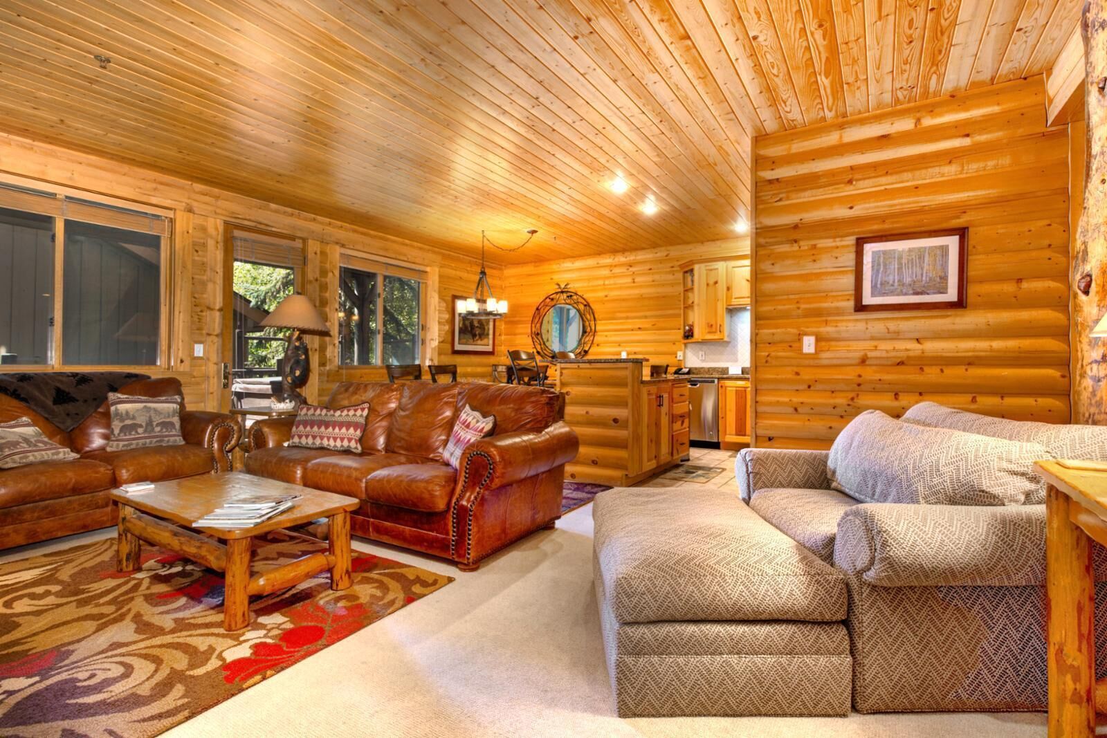 A log cabin interior with a living room featuring a leather sofa, a wooden coffee table, and a patterned rug.