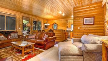 A log cabin interior with a living room featuring a leather sofa, a wooden coffee table, and a patterned rug.