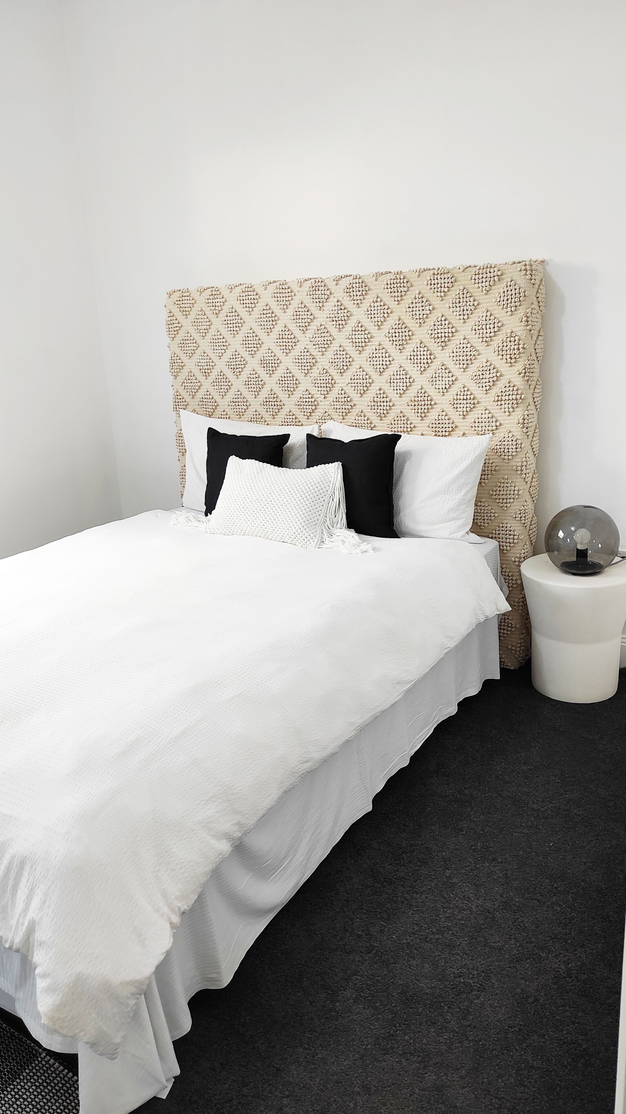 Un lit bien fait, avec une couette blanche et des oreillers, une tête de lit à motifs et une table de chevet avec une lampe.