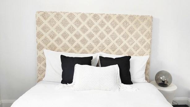Cama com cabeceira estampada, almofadas brancas e pretas e mesa de cabeceira com um objeto esférico.
