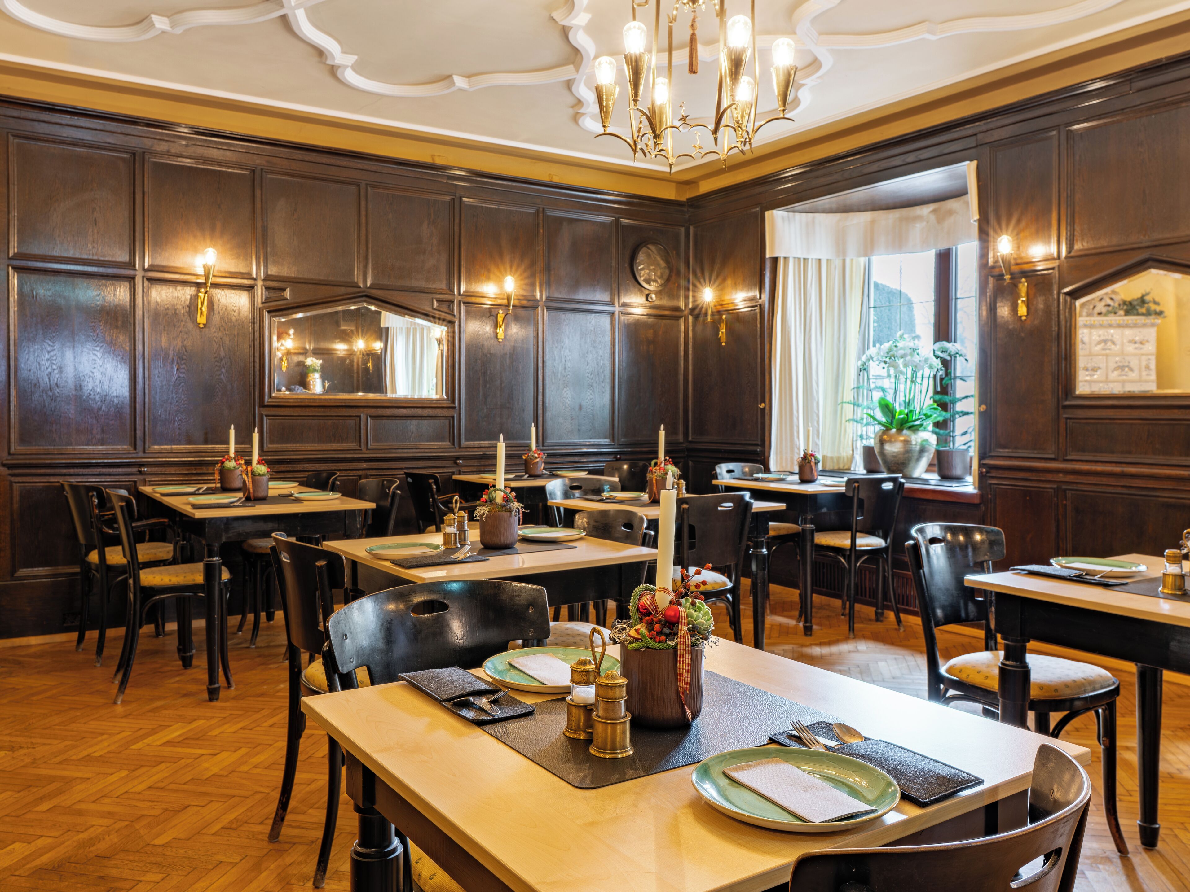 A restaurant interior with wooden paneling, chandeliers, and tables set for dining.