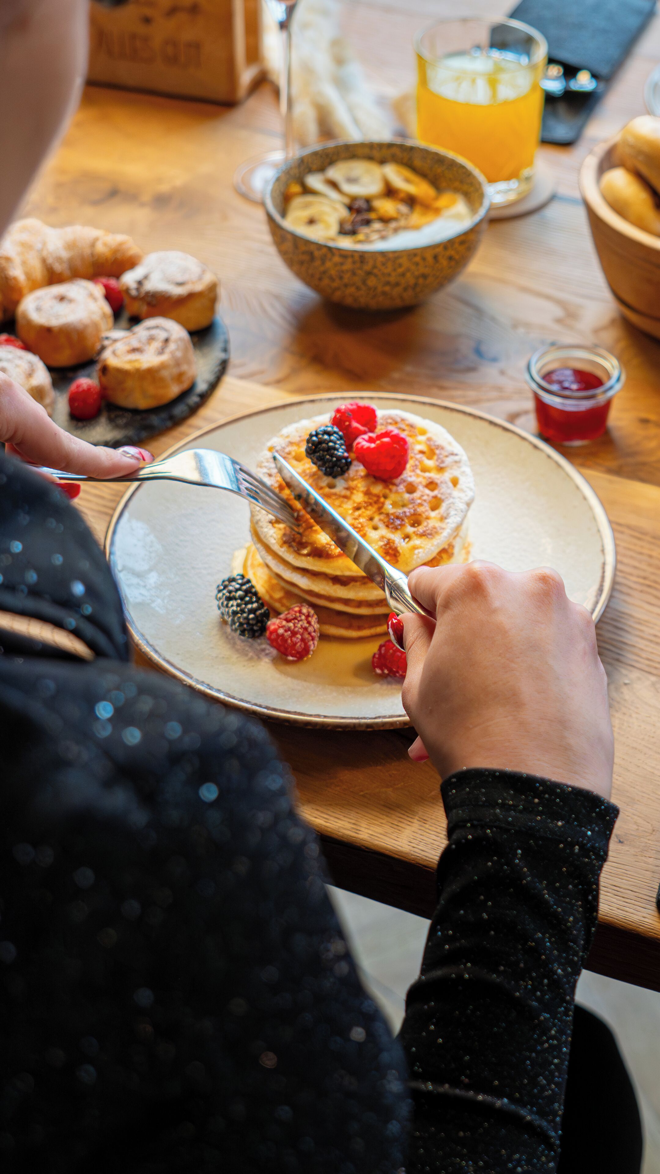 Un desayuno con tortitas cubiertas de frutos rojos, un vaso de zumo de naranja y un tazón de cereales.