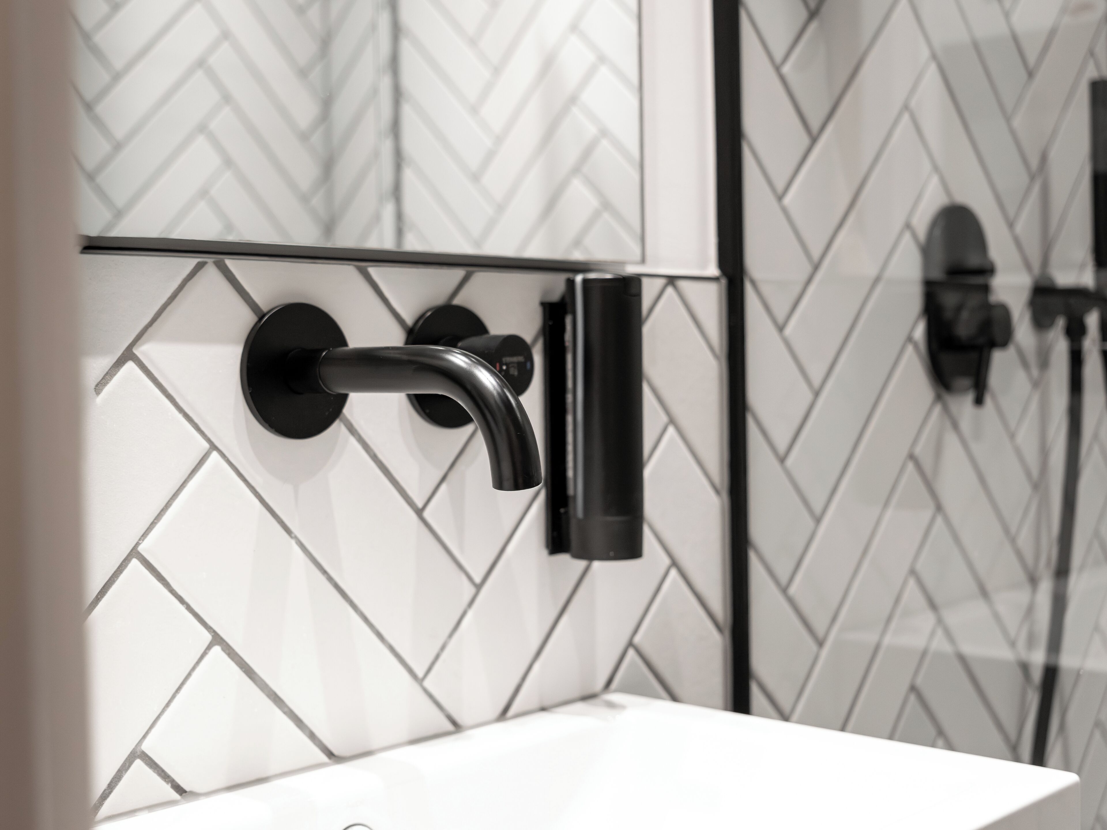 Een badkamer met een wit wastafel, een zwarte kraan en een wand betegeld met een herringbone-patroon.
