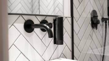 Een badkamer met een wit wastafel, een zwarte kraan en een wand betegeld met een herringbone-patroon.