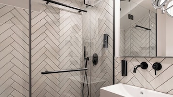 Un baño moderno con salpicadero de baldosas en espiga, cabina de ducha de cristal, lavabo blanco y espejo.