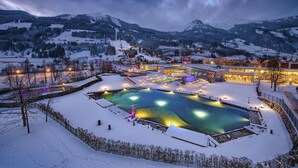 Ett snötäckt utomhuspoolområde med omgivande byggnader och berg i bakgrunden.