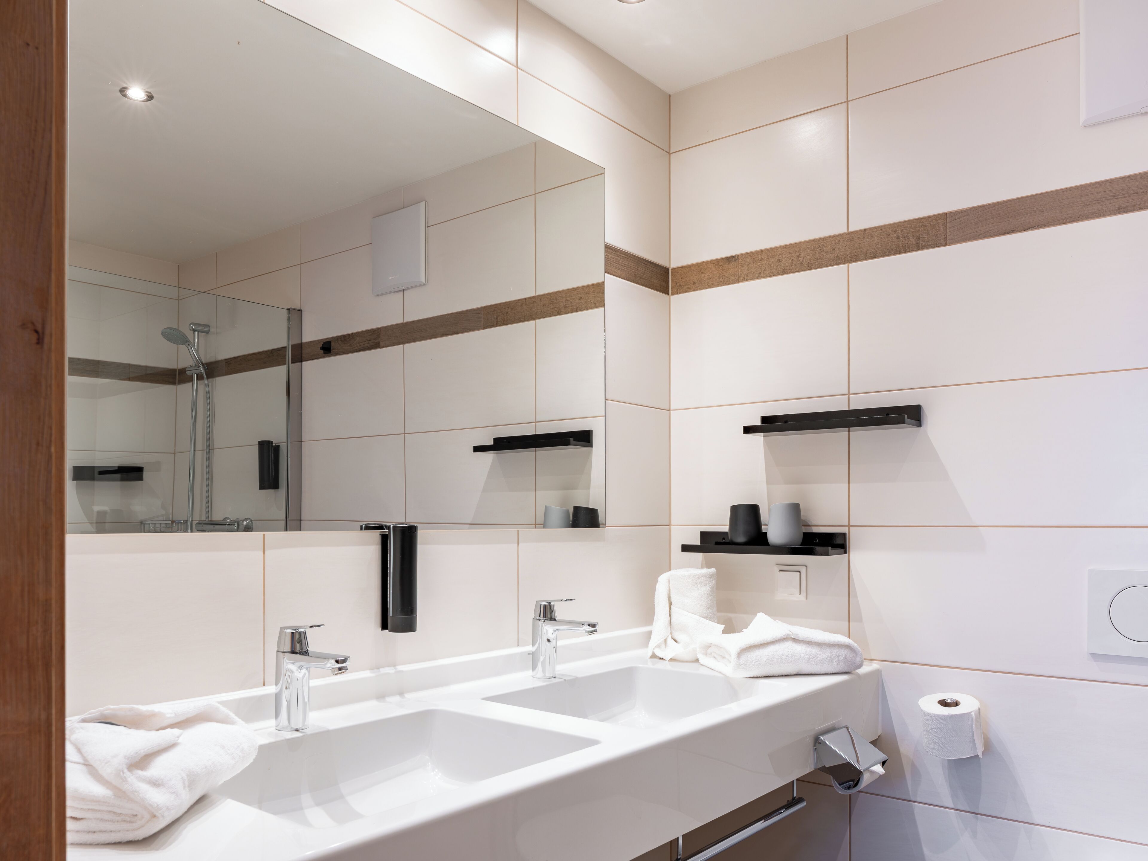 A modern bathroom with two sinks, a large mirror, and a shower.