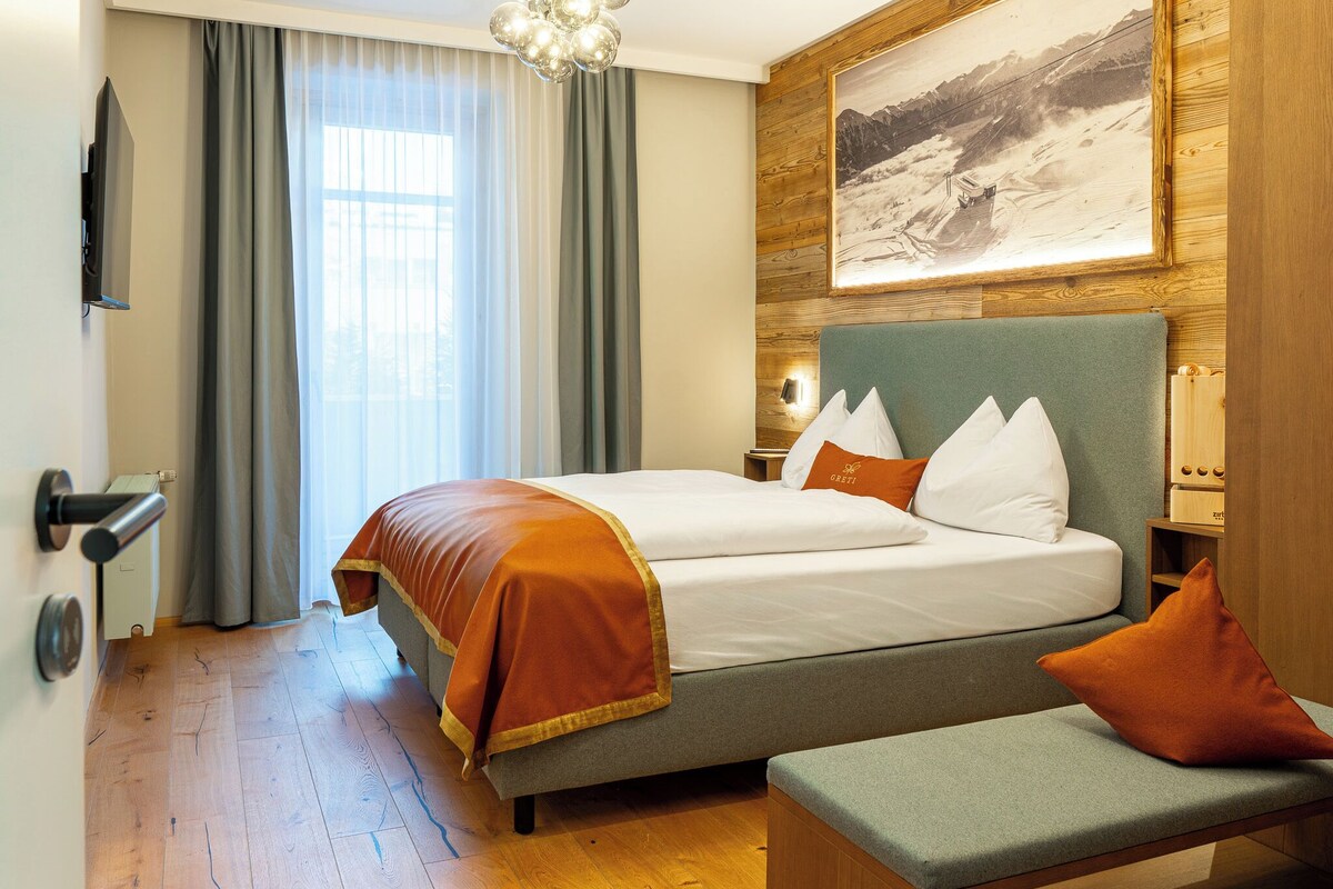 Een hotelkamer met een bed, een bankje, een schilderij aan de muur en een raam met gordijnen.