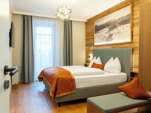 Habitación de hotel con cama, un banco, un cuadro en la pared y una ventana con cortinas.