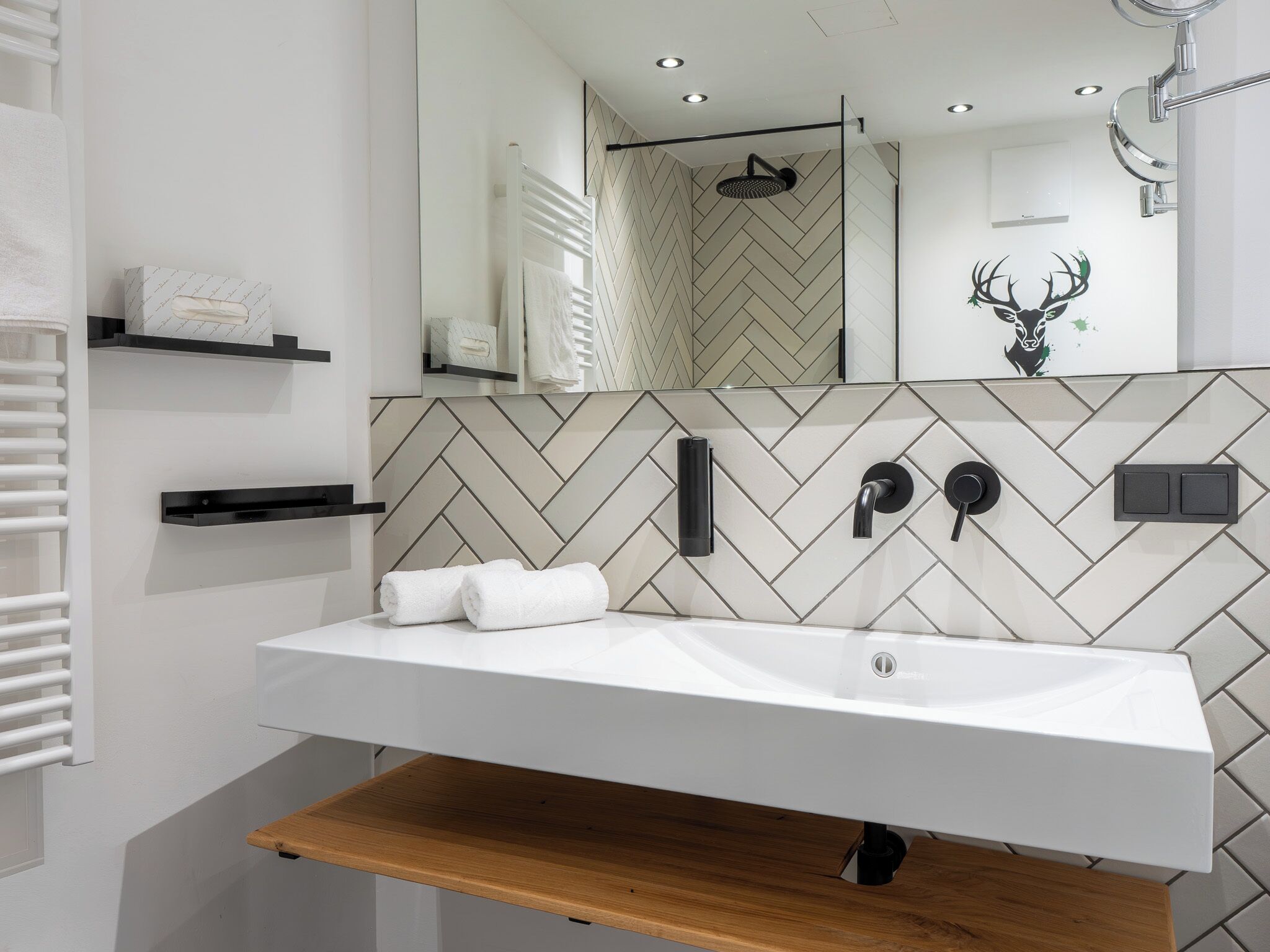 Un baño moderno con un lavabo blanco, un espejo, una ducha y un revestimiento de pared con diseño de espiga.