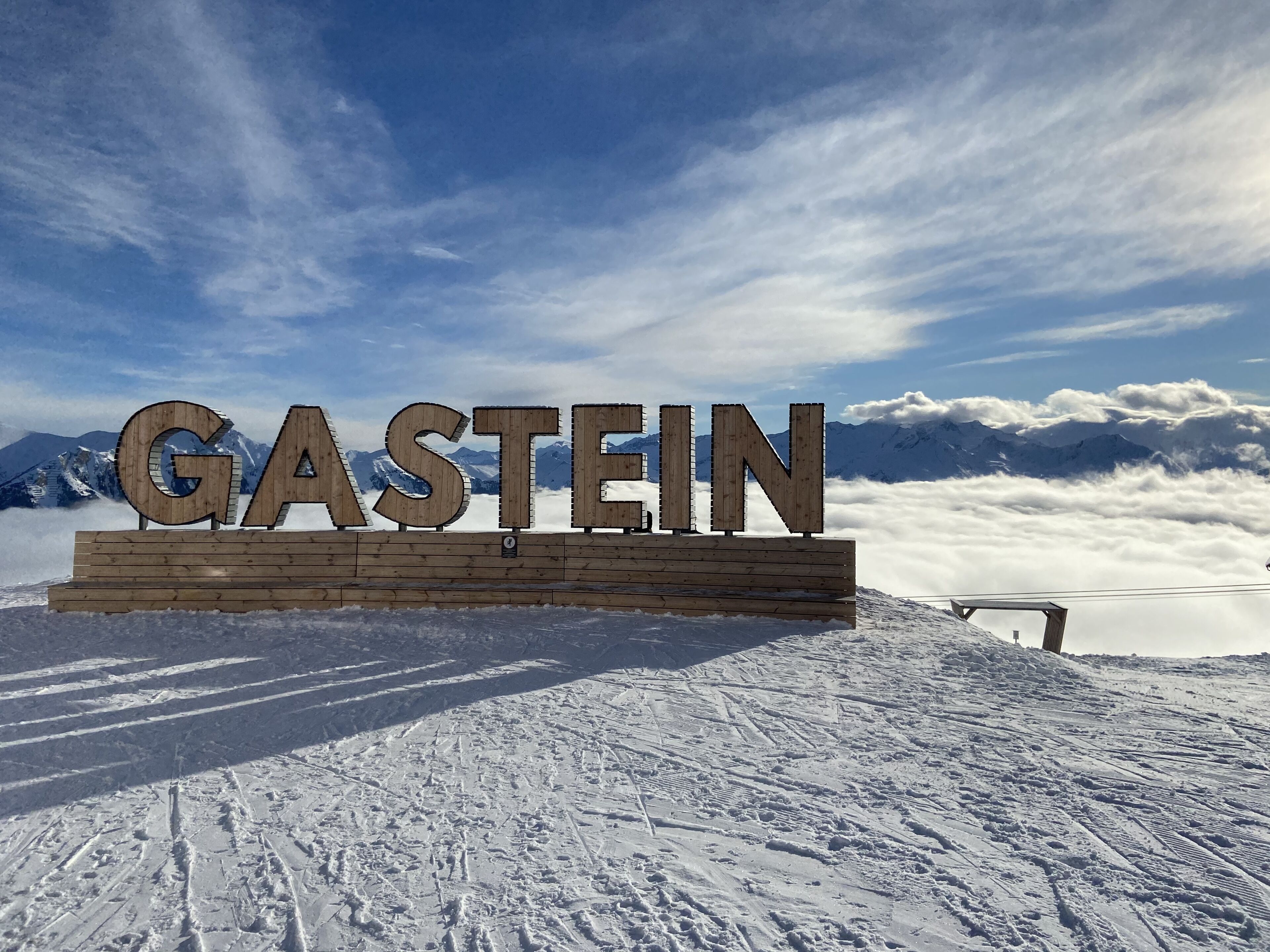 Un letrero de madera con la palabra 'GASTEIN' en una ladera nevada de montaña.