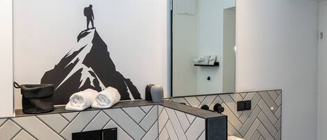 Un baño moderno con salpicadero de baldosas en patrón herringbone, un espejo grande y un adhesivo mural con forma de montaña.