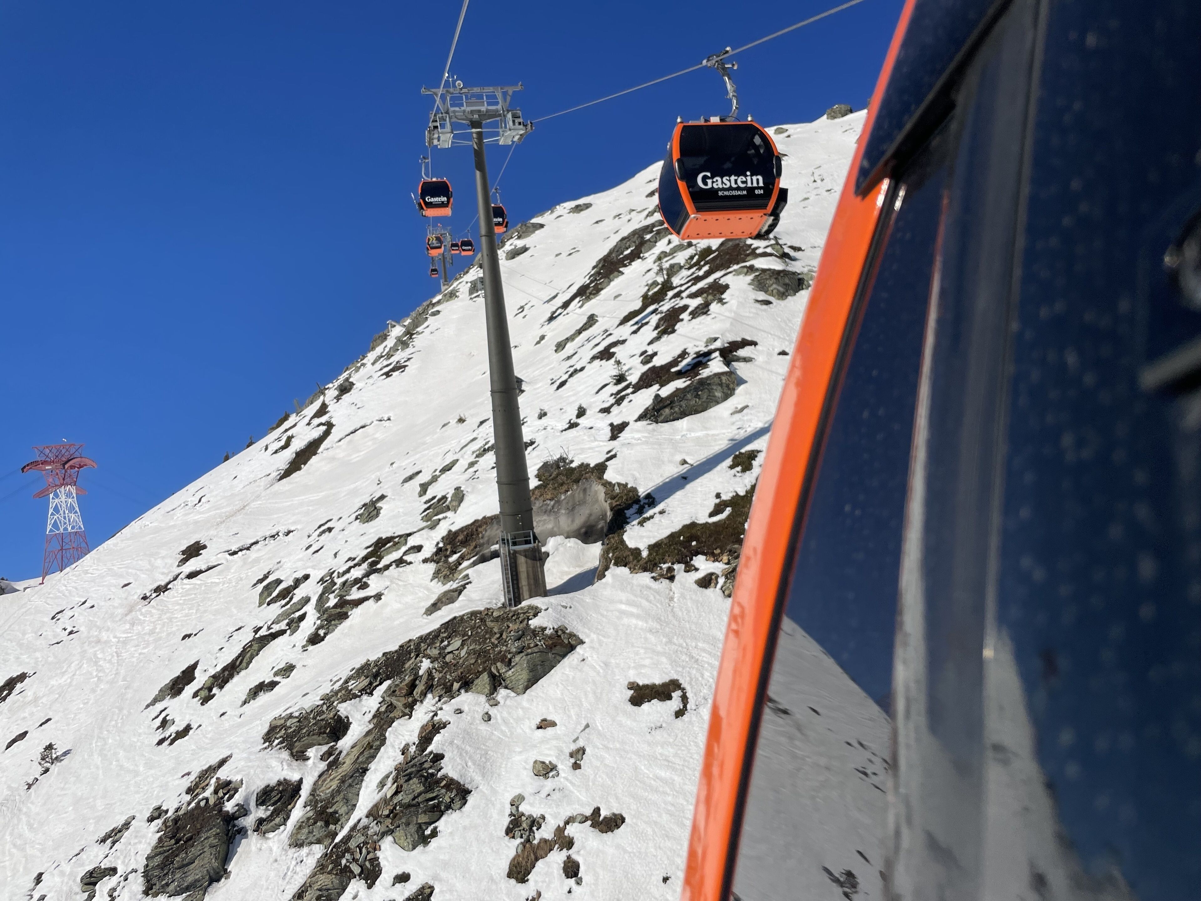 Un sistema de teleférico con asientos que llevan la etiqueta 'Gastein' en una montaña nevada.