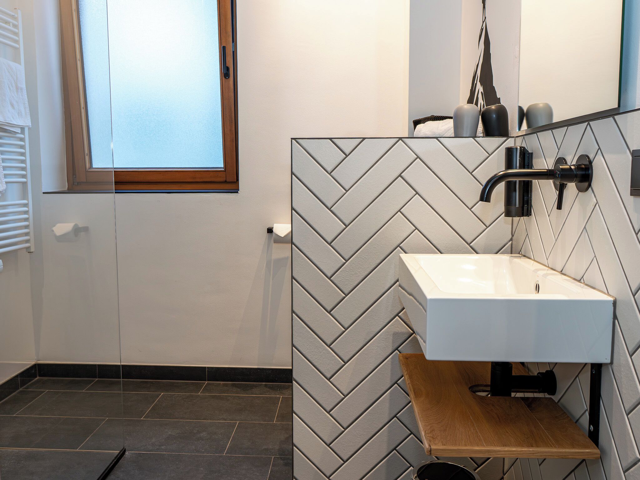 A modern bathroom with a herringbone-patterned wall, a white sink, and a wooden vanity.